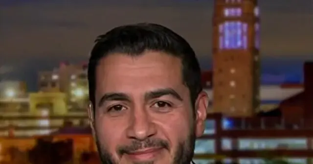 The image shows a man with a beard and short hair, smiling, with a cityscape and a tall tower in the background.