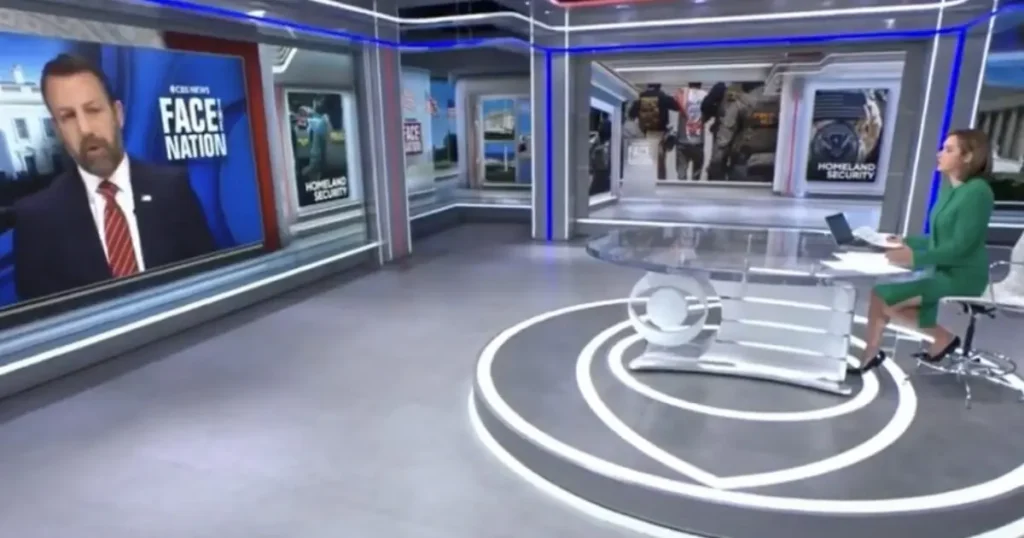 The image shows a news studio with a host seated at a desk, and a large screen displaying a segment titled "Face the Nation."