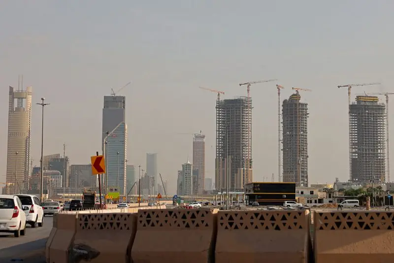 The image shows a bustling urban landscape with multiple high-rise buildings under construction, featuring cranes and modern architecture, set against a hazy sky.