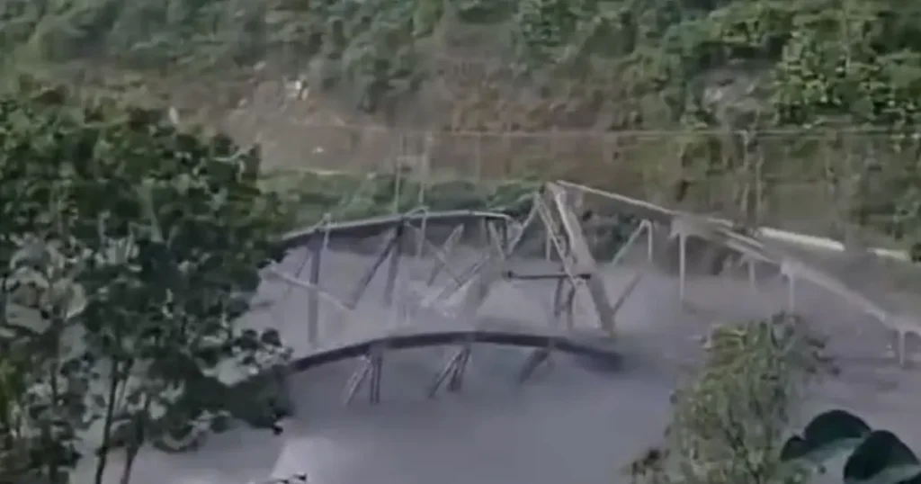 The image shows a damaged structure, possibly a bridge, with visible structural failure and debris scattered around, indicating a significant incident.