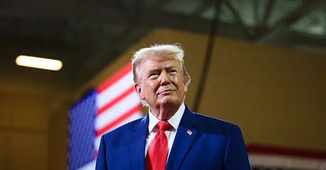 The image shows a person in a blue suit and red tie standing in front of an American flag.