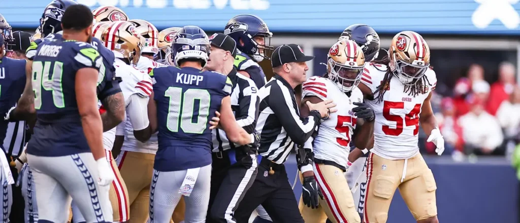 A football referee attempts to separate players from the Seattle Seahawks and the San Francisco 49ers during a game.