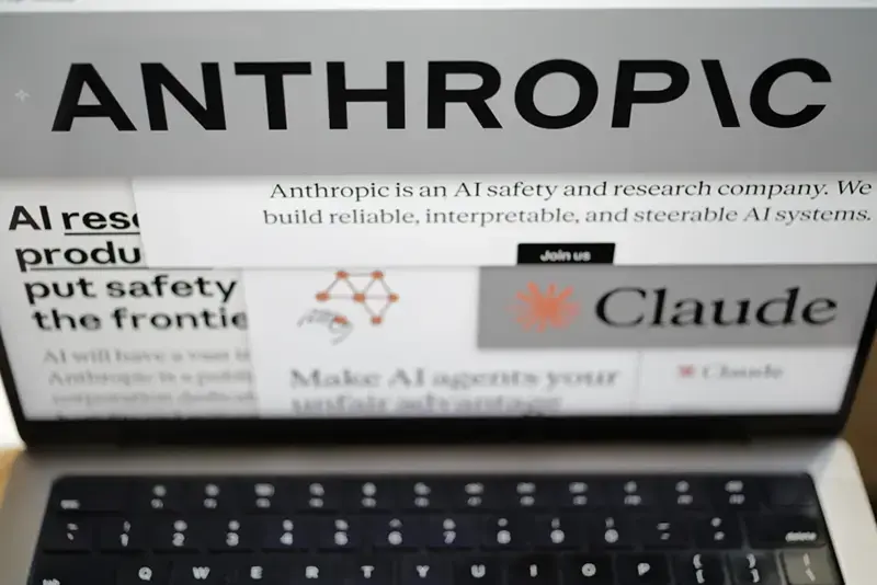 The image shows a laptop screen displaying the website for Anthropic, an AI safety and research company, with the text "Claude" and a slogan about making AI agents your unfair advantage.