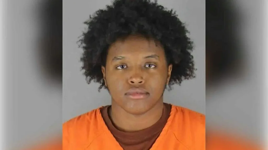 The image shows a person in an orange prison uniform against a plain background.