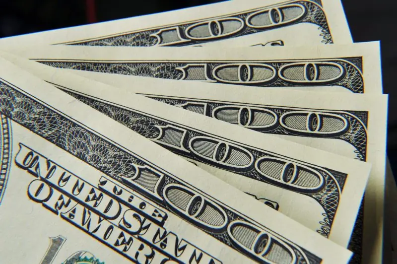 The image shows a close-up of several hundred-dollar bills fanned out, highlighting the intricate security features and denominations.