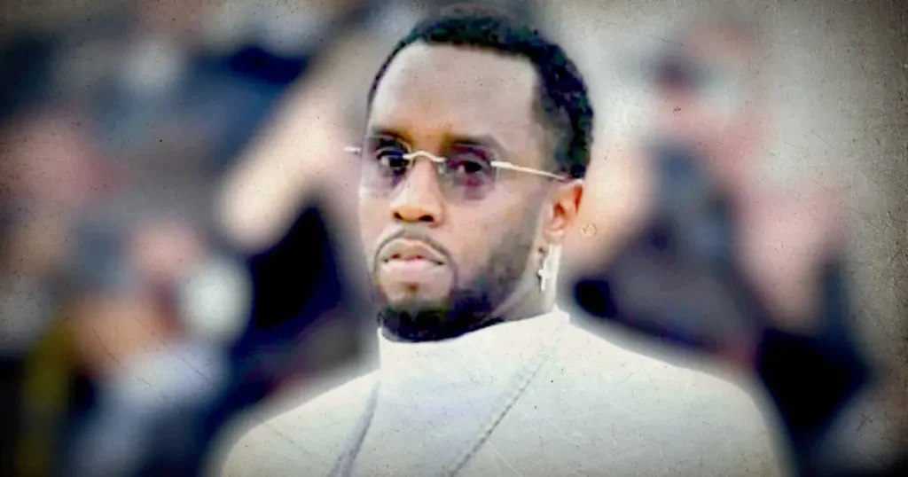 The image appears to be a stylized, possibly filtered or edited, photo of a man wearing glasses and a light-colored shirt, with a blurred background that suggests a crowd or public setting.