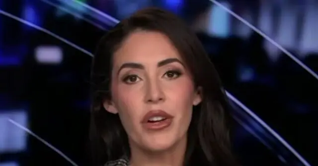 The image shows a news anchor in a studio setting with a blurred background of lights and lines.