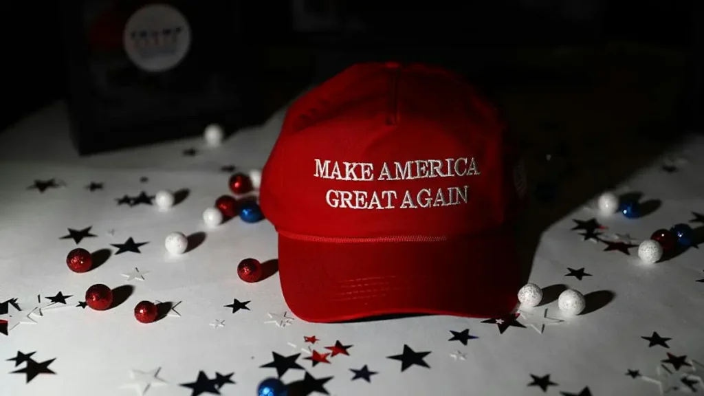 A red baseball cap with the phrase "MAKE AMERICA GREAT AGAIN" is displayed on a table adorned with patriotic decorations.