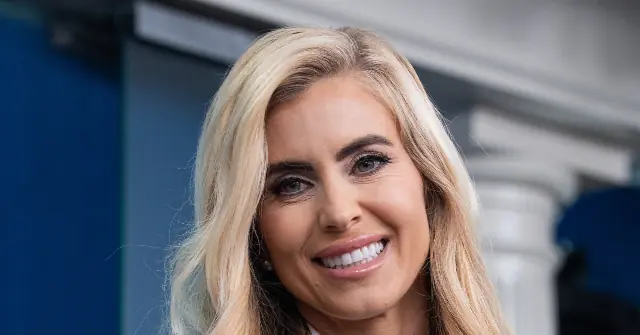 The image shows a person with long blonde hair smiling, with a blue and white background.