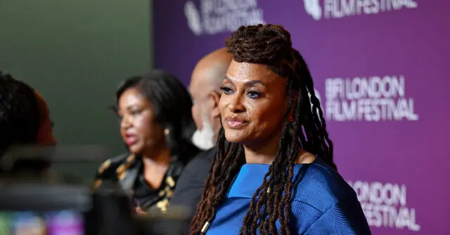 A woman with long braided hair is seen at the BFI London Film Festival, standing in front of a purple backdrop.