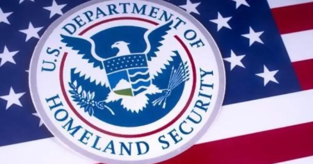 The image shows the seal of the U.S. Department of Homeland Security against the backdrop of the American flag.