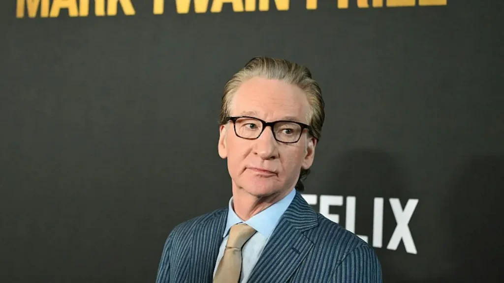 The image shows a man in a suit and tie standing in front of a backdrop with the words "MARK TWAIN" and "NETFLIX" visible.
