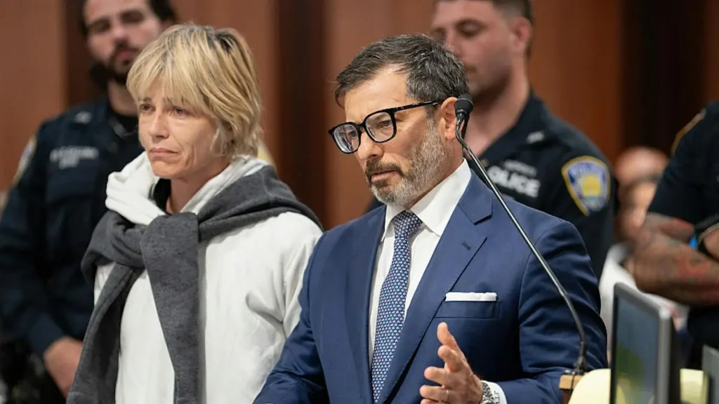A man in a suit speaks into a microphone while a woman in a hoodie stands beside him in what appears to be a courtroom setting.