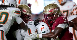 A football player in a white uniform is tackled by two players in maroon uniforms during a game.