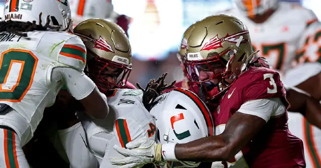 A football player in a white uniform is tackled by two players in maroon uniforms during a game.