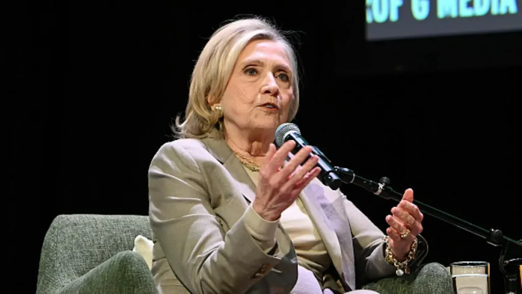 The image shows a person speaking into a microphone during a formal discussion or interview setting.