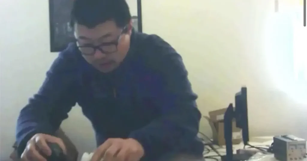 A person wearing glasses is seated at a table, seemingly engaged in an activity involving a small object in their hands.