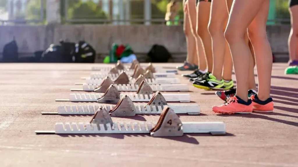 Athletes prepare for a race at a starting line with numbered blocks on a track.