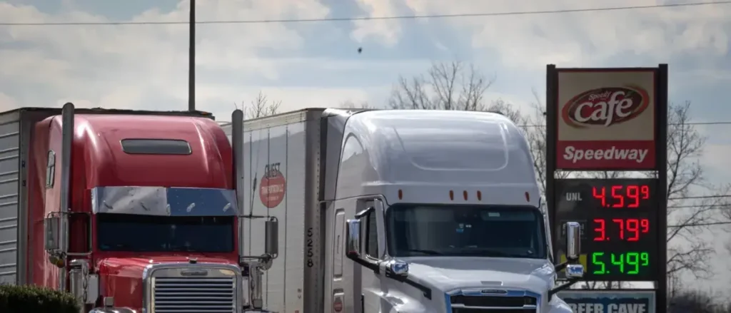 Two semi-trucks are parked at a Speedway gas station with fuel prices displayed on the sign.