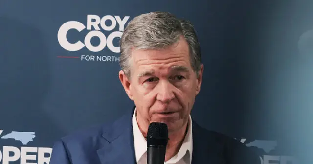 The image shows a man speaking into a microphone in front of a backdrop with the text "ROY COOPER FOR NORTH."