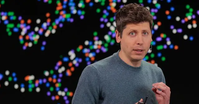 The image shows a person speaking in front of a colorful, abstract background.