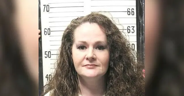 The image appears to be a mugshot of a woman with long, curly hair, standing in front of a height chart.