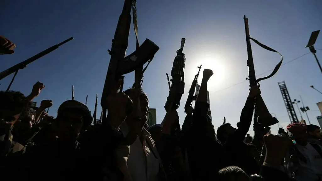 A group of people raise their weapons and fists in a demonstration under a bright sun.