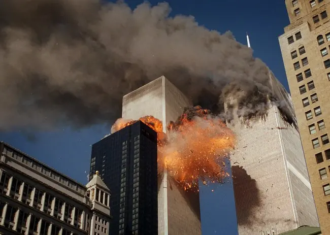 The image depicts a dramatic explosion and collapse of a high-rise building, with thick smoke and debris filling the sky.