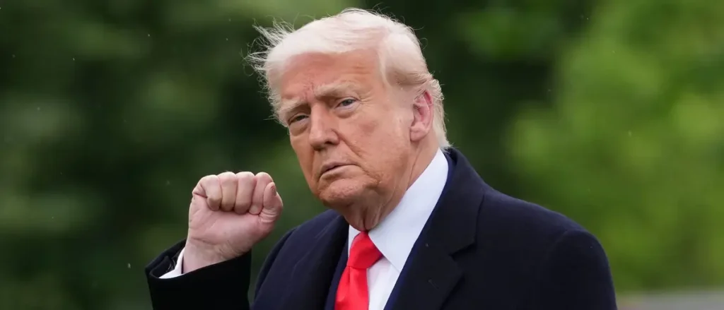 The image shows a person in a suit and red tie, with a fist raised, set against a blurred green background.