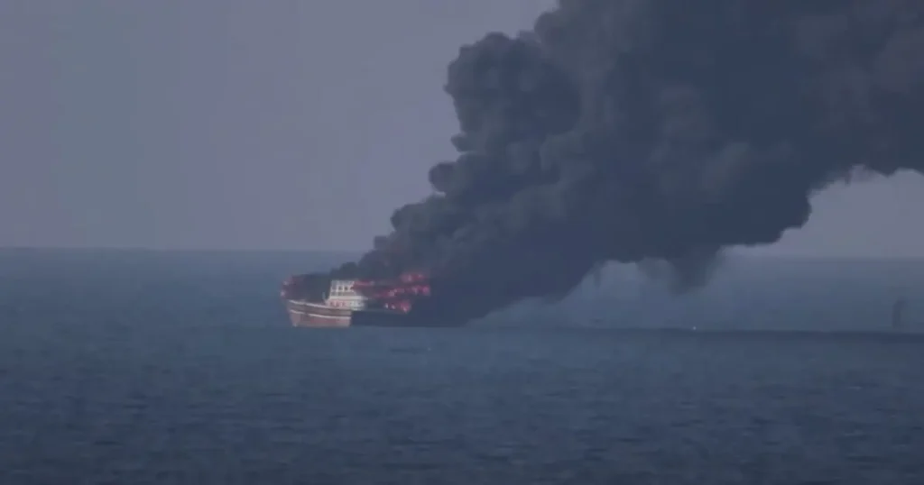 A ship is engulfed in flames and emitting thick black smoke into the air.
