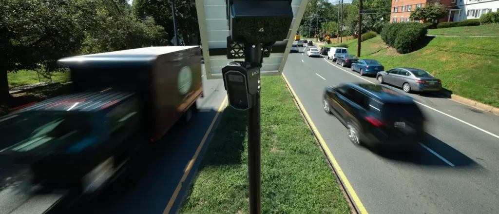 A speed camera is positioned on the side of a road, capturing vehicles as they pass by.