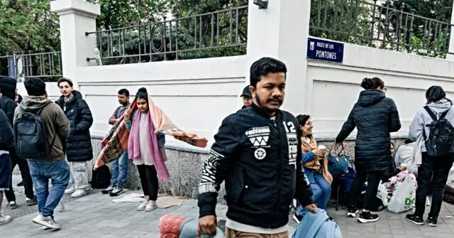 A group of people, some carrying bags and belongings, are gathered outside a building labeled "Paseo de los Pontones," possibly indicating a location related to immigration or assistance.
