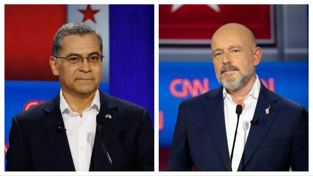 The image shows two men participating in a political debate, with one wearing glasses and the other sporting a beard, both dressed in suits and standing in front of a CNN backdrop.