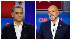 The image shows two men participating in a political debate, with one wearing glasses and the other sporting a beard, both dressed in suits and standing in front of a CNN backdrop.