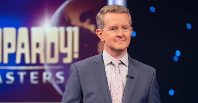 The image shows a man in a suit and tie standing in front of a "Jeopardy! Masters" backdrop.