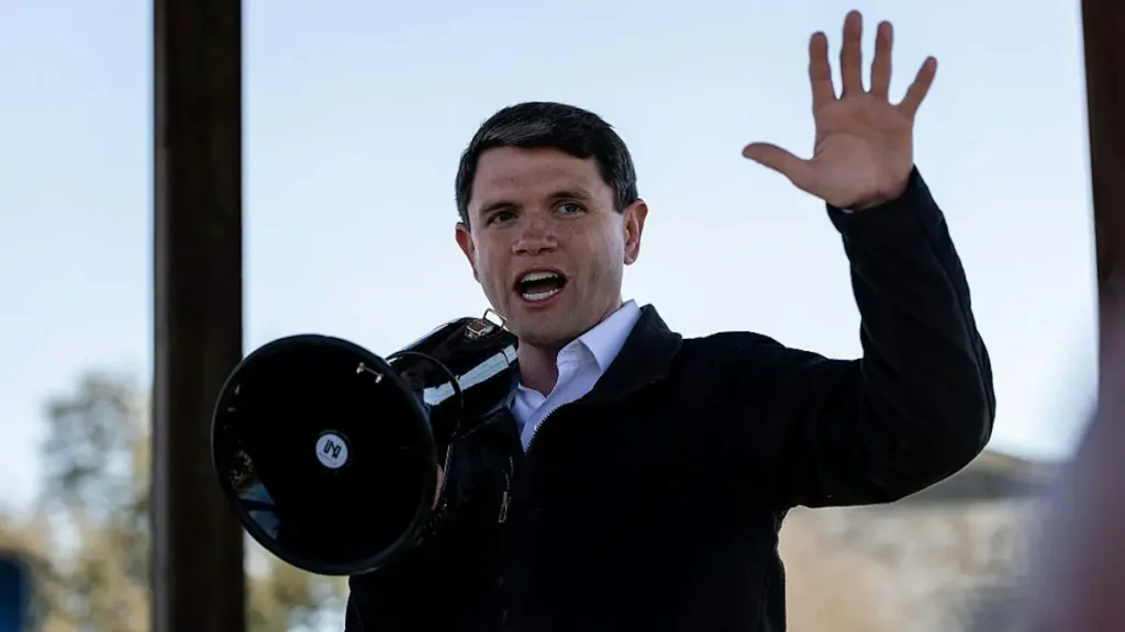 A man is speaking passionately into a megaphone while raising his other hand in a gesture of emphasis.