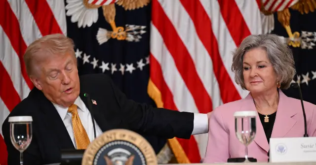 The image shows a formal setting with two individuals seated at a table, one of whom is gesturing with their hand, with American flags and presidential seals in the background.