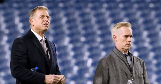 Two men stand side by side on a sports field, with a blurred stadium crowd in the background.