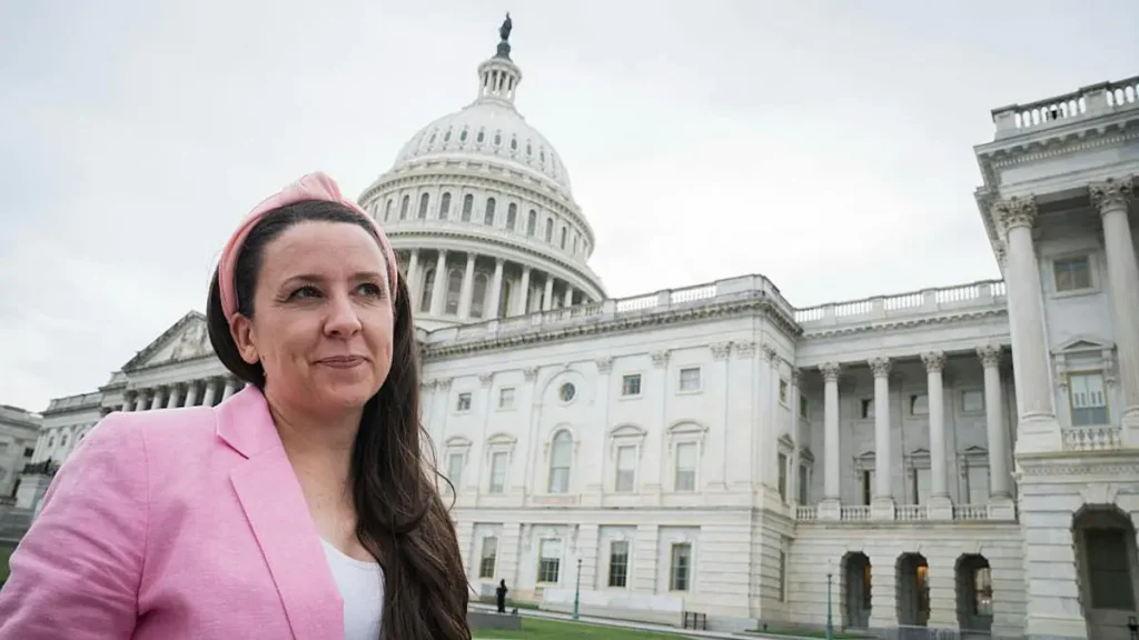 A woman in a pink blazer stands in front of the U.S. Capitol building.
