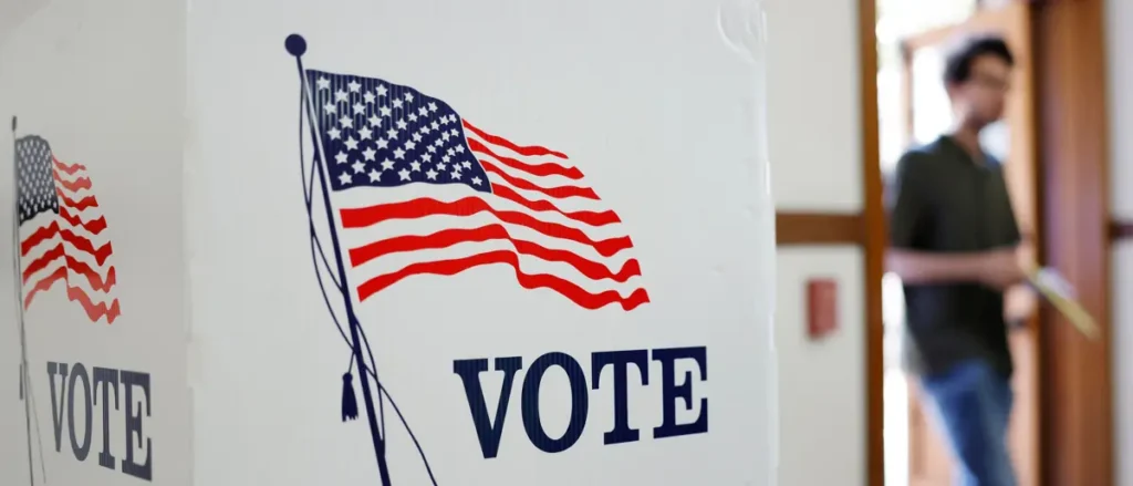 A person walks into a voting booth with an American flag and "VOTE" signs prominently displayed.