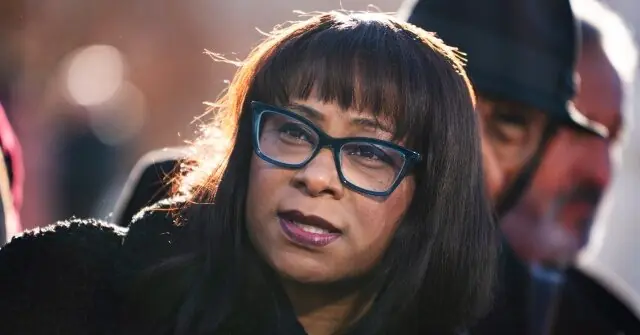 The image shows a person wearing glasses and a black coat, with sunlight casting a warm glow on their hair.