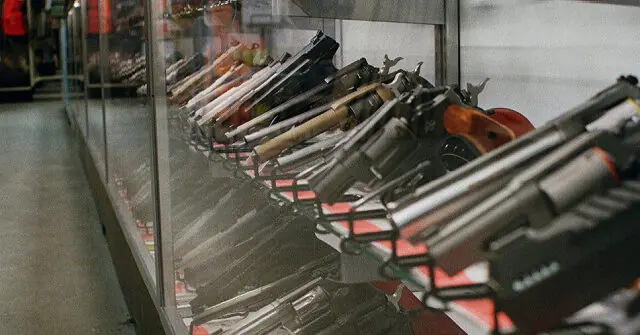 The image shows a display case in a store containing a variety of firearms.