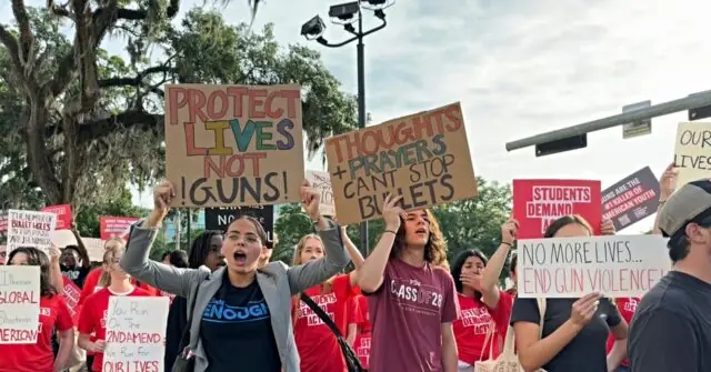 The photo depicts a group of protesters holding signs advocating for gun control and an end to gun violence.