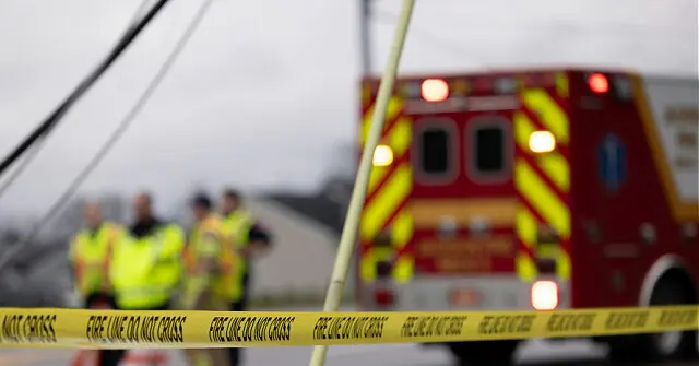 The image shows a scene with emergency responders and an ambulance, cordoned off by yellow "Fire Line Do Not Cross" tape.