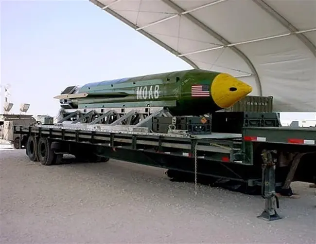 The image shows a large military bomb, labeled "MOAB," being transported on a flatbed truck under a tent.