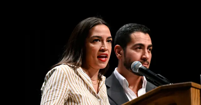 A woman speaks into a microphone at a podium, with a man standing beside her.
