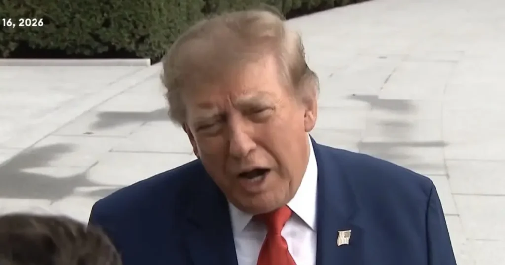 The image shows a man in a dark suit and red tie speaking outdoors, with a date of "16, 2026" visible in the corner.