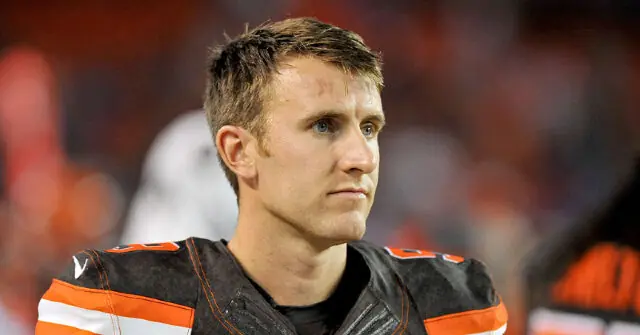 The image shows a football player in a black and orange uniform, looking off to the side with a focused expression.