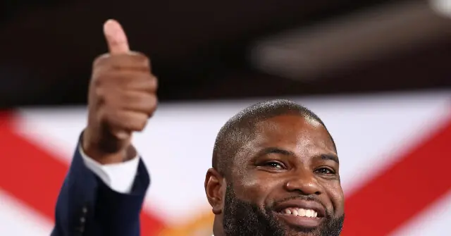 A man gives a thumbs-up gesture in front of an American flag.