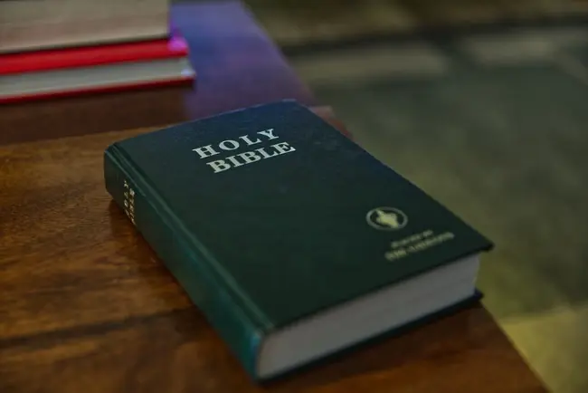 The image shows a close-up of a green Holy Bible placed on a wooden surface, with a blurred background.